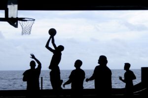 Die Silhouette von Basketballern, die am Meer auf einen Korb spielen
